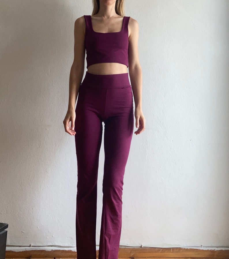 May include: A two-piece outfit in a deep purple color. The top is a sleeveless crop top with a square neckline. The pants are a high-waisted, wide-leg style.