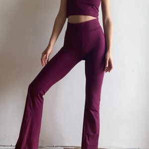 Può includere: Un completo in due pezzi di colore bordeaux scuro. La parte superiore è un top corto a spalline con scollo quadrato. I pantaloni sono pantaloni a zampa di elefante a vita alta.