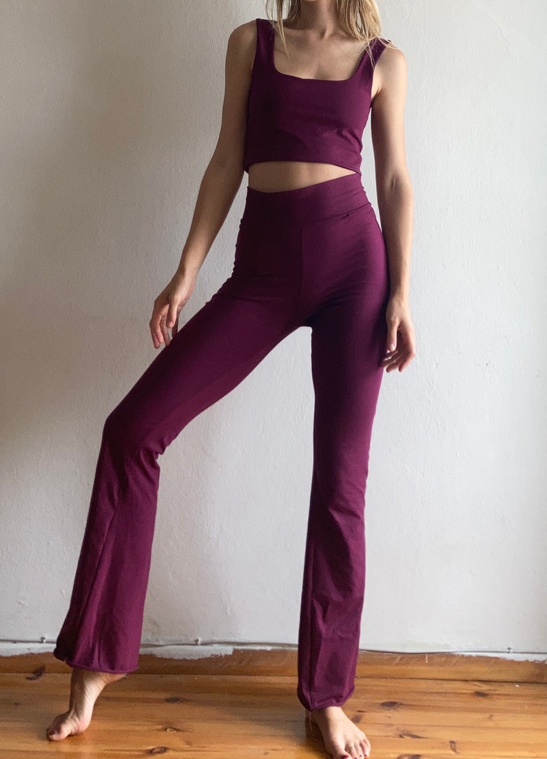 May include: A two-piece outfit in a deep burgundy color. The top is a cropped tank top with a square neckline. The pants are flared-leg pants with a high waist.
