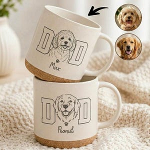 May include: Two white ceramic mugs with a cork base, stacked. Each mug has a black line drawing of a dog's face, the word "DAD" in block letters, and a paw print. One mug says "Max" and the other says "Peanut".