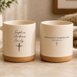 May include: Two off-white ceramic mugs with cork bottoms. One mug has the names "Sophia, Andrew, Emily" and a cross. The other mug has the text "fatherhood is kingdom work" and a cross. Both mugs have a curved handle.