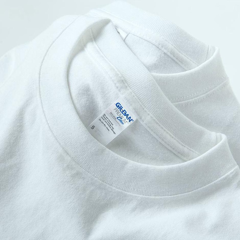 May include: Close-up of two white crew neck t-shirts. The Gildan Premium Cotton label is visible on one shirt, with the size "S" printed on the label. The shirts are made of a soft, likely cotton material.