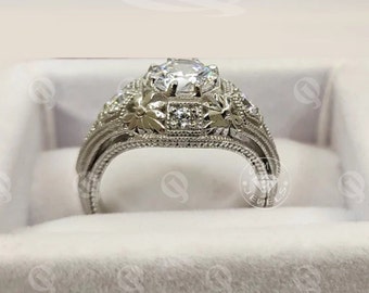 May include: A silver ring with a large, round, clear center stone and smaller clear stones on the band. The band is decorated with intricate floral designs.