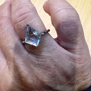 May include: A silver ring with a clear, faceted, kite-shaped gemstone. The gemstone has black and gray inclusions.