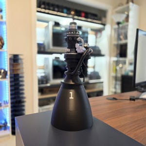 May include: A black and silver model rocket engine with a nozzle and the number "1" printed on the side.