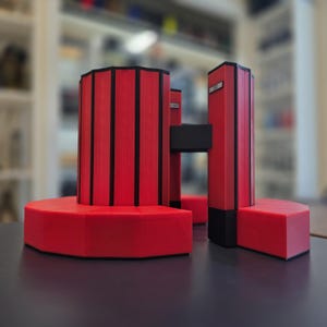 May include: A modern, geometric sculpture in red and black. The piece features a circular base, vertical columns, and connecting elements. The design incorporates bold lines and shapes, creating a striking visual contrast. The sculpture is a vibrant accent piece.