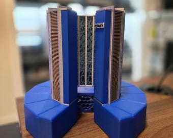 May include: A blue and tan model of a Cray supercomputer. The model has two tall blue towers with tan vents and the word "CRAY" on the side. The base is blue and octagonal. The model is on a wooden surface.