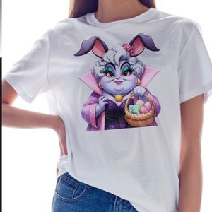 May include: A white t-shirt with a cartoon image of a purple bunny wearing a pink and black dress and holding a basket of colorful Easter eggs.
