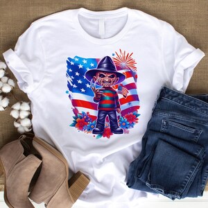 May include: White t-shirt featuring a cartoon character with a hat and striped sweater, holding a flag in front of an American flag design. The shirt is paired with blue jeans and tan ankle boots. The design includes flowers and fireworks.