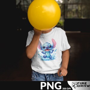 Puede incluir: Una camiseta blanca con un personaje de dibujos animados azul con orejas rosas, ojos azules y una gran sonrisa. El personaje est&aacute; de pie en un charco de agua con salpicaduras azules y blancas. La camiseta est&aacute; siendo sostenida por un ni&ntilde;o.