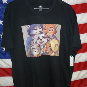 May include: Black t-shirt featuring a colorful graphic of animated anthropomorphic animals. The graphic includes a fox, a rabbit, a wolf, and other characters. The shirt is hanging against a backdrop of an American flag.