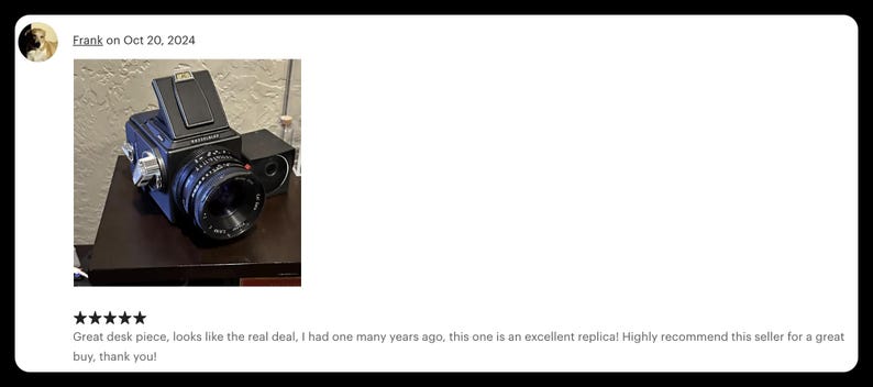 May include: A black vintage camera with a large lens and a top-mounted viewfinder. The camera is on a dark surface. The image includes text that says "Frank on Oct 20, 2024" and a customer review.