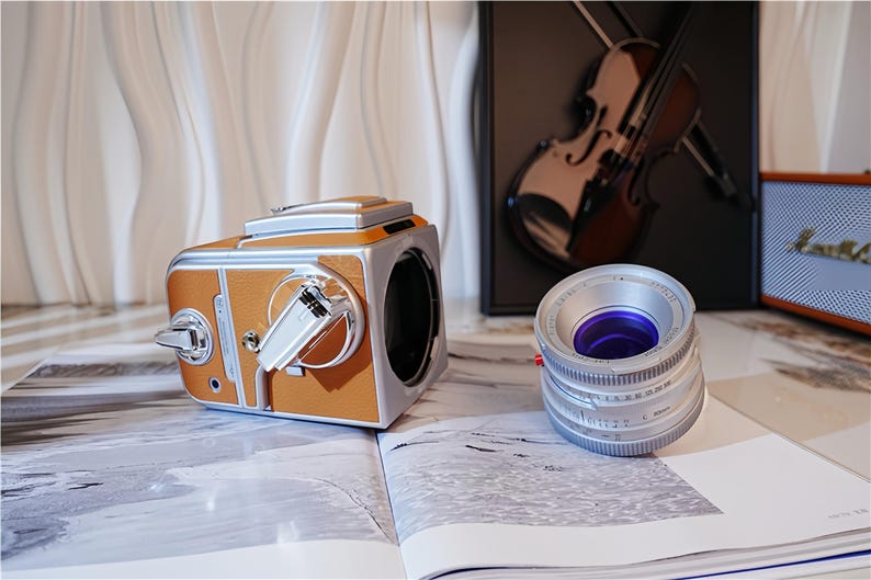 May include: A vintage-style camera with a brown leather-like exterior and silver accents sits on an open book. A silver camera lens with a purple interior is next to the camera. The scene includes a violin and a speaker.