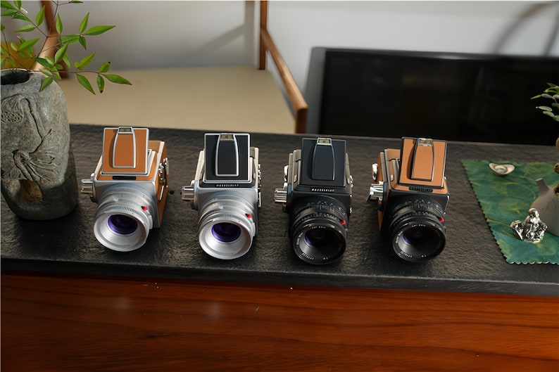 May include: Four vintage-style cameras with silver bodies and leather accents are displayed. Two have brown leather, one has black, and one has silver. Each camera has a prominent lens and a top-mounted viewfinder.