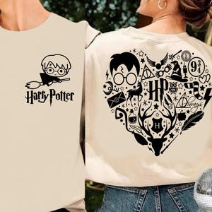 May include: A cream-colored t-shirt with a black graphic of Harry Potter on a broom and the text "Harry Potter". The back of the shirt features a heart-shaped design with various Harry Potter symbols and the word "Always".