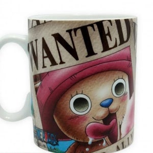 May include: A white ceramic mug with a brown, pink, and blue cartoon character on it. The character is a bear with a pink hat and a long tongue sticking out. The mug has the word "WANTED" printed on it in brown letters.