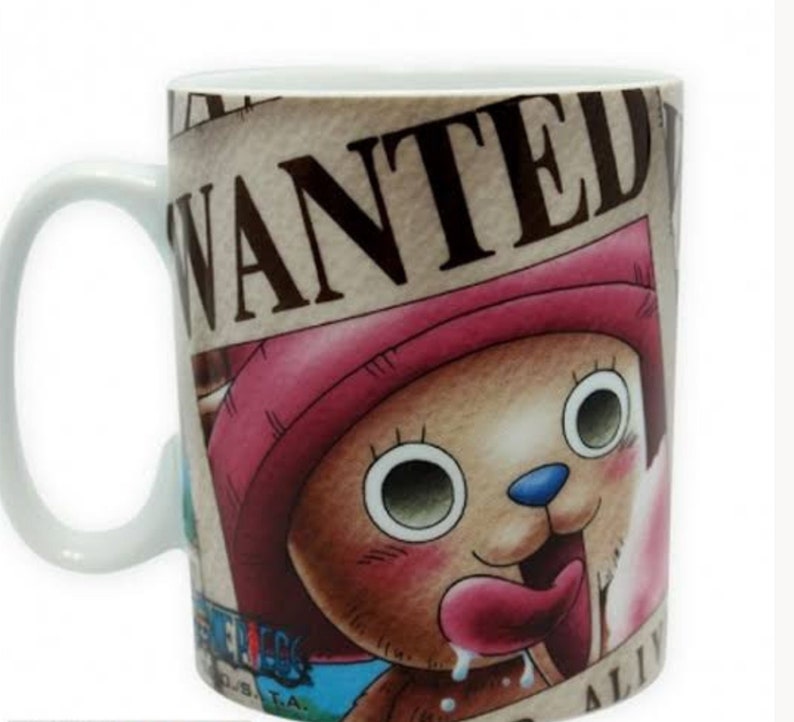 May include: A white ceramic mug with a brown, pink, and blue cartoon character on it. The character is a bear with a pink hat and a long tongue sticking out. The mug has the word "WANTED" printed on it in brown letters.