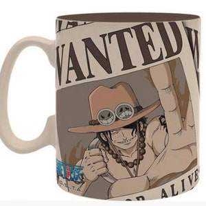 May include: A white ceramic mug with a brown handle. The mug features a wanted poster with a cartoon image of a man with brown hair, a brown hat with goggles, and a beaded necklace. The poster says "WANTED" at the top and "DEAD OR ALIVE" at the bottom.