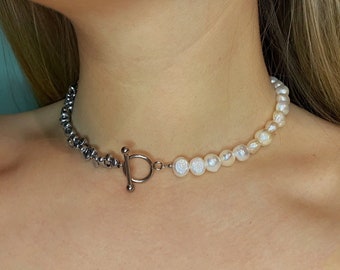 May include: A silver chain necklace with a toggle clasp connects to a strand of white pearls. The necklace is worn on a person's neck.