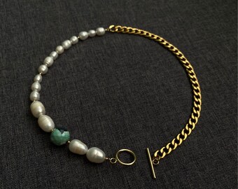 May include: A gold chain necklace with a pearl and green gemstone pendant. The necklace has a toggle clasp.