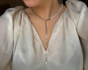 May include: A silver chain necklace with a single pearl pendant. The chain is made of linked circles and the pearl is white.