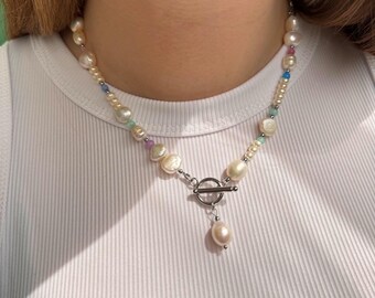 May include: A white pearl necklace with colorful beads and a silver toggle clasp. The necklace has a single pearl drop pendant.