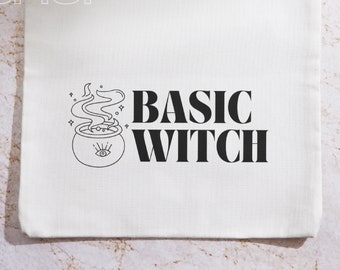 Könnte beinhalten: Beige Canvas-Tragetasche mit dem Text "BASIC WITCH" in fetten schwarzen Buchstaben. Links vom Text befindet sich eine schwarze Illustration eines Kessels mit Dampf und einem Auge. Die Worte "HEY BABE SHOP" sind oben in Hellgrau gedruckt.