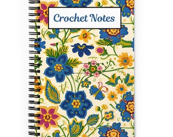 Pode incluir: Caderno espiralado creme com capa com padrão floral em azul, amarelo e roxo. As palavras "Crochet Notes" são exibidas num retângulo branco. Encadernação em espiral preta.