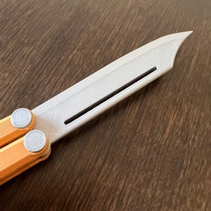 May include: A silver butterfly knife with a textured blade and orange handles. The knife is partially open, showing the mechanism.