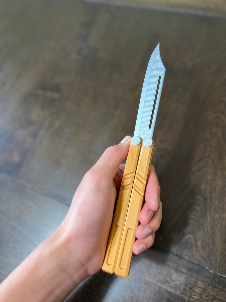May include: A wooden butterfly knife with a silver blade. The knife is closed and being held in a hand.