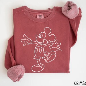 May include: A maroon sweatshirt with a white outline of Mickey Mouse on the front. The sweatshirt has a crew neck and long sleeves.