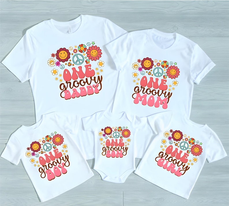 May include: Set of five white t-shirts with a groovy 70s theme. The shirts feature a peace sign, flowers, and the text "One groovy [name]" in pink and brown lettering.