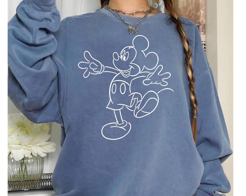 May include: A blue sweatshirt with a white outline of Mickey Mouse in a walking pose. The sweatshirt has a relaxed fit and long sleeves.