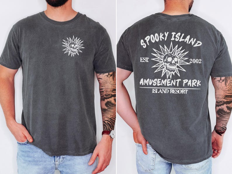 May include: Dark gray t-shirt with a white skull and sunburst graphic on the front and back. The back of the shirt reads "Spooky Island Amusement Park Island Resort" with the year "2002".