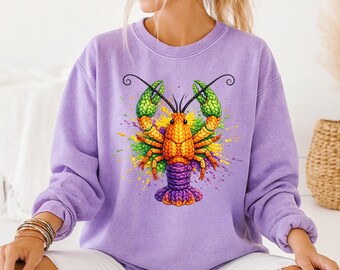 May include: A light purple sweatshirt featuring a vibrant, colorful illustration of a crawfish. The crawfish is depicted with orange, yellow, green, and purple accents, with a splash of paint effect around it. The sweatshirt has long sleeves and a crew neck.