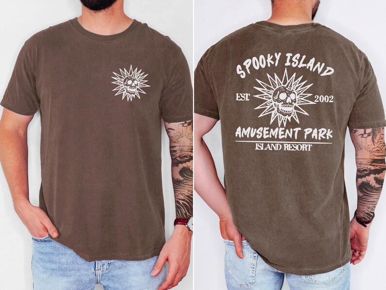 May include: Brown t-shirt with a white skull and sunburst graphic on the front and back. The back of the shirt reads "Spooky Island Amusement Park Island Resort" with "Est 2002".