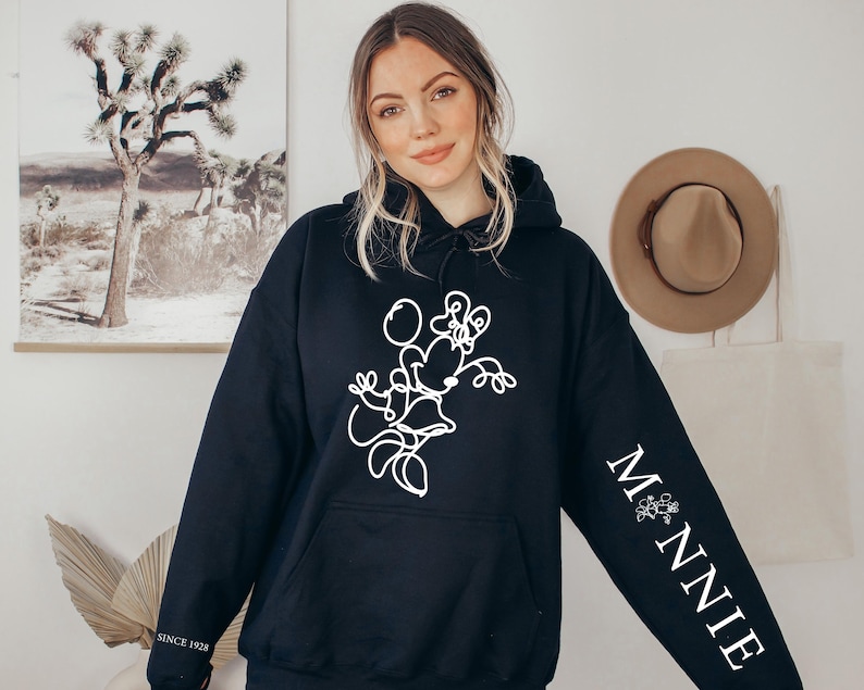 May include: Black hooded sweatshirt featuring a white line drawing of Minnie Mouse on the front. The right sleeve has the word "MINNIE" in white, with a floral design. The text "SINCE 1928" is printed on the left sleeve.