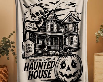May include: A cream-colored Halloween-themed blanket featuring a black and white illustration of a haunted house, skull, bats, and a jack-o'-lantern. Text includes "It's a Scream!" and "We dare you to visit the Haunted House."