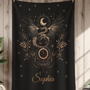 May include: Black tapestry with a golden dragon design, a crescent moon, and the name "Sophia" in elegant script. The dragon has outstretched wings and is surrounded by celestial elements and botanical details. The tapestry is hanging on a wooden background.