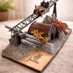 May include: A miniature roller coaster model with a brown train car ascending a black track. The track leads to a weathered brown building with a curved roof. The base features rock formations and a small sign with etched text. Decorative model.