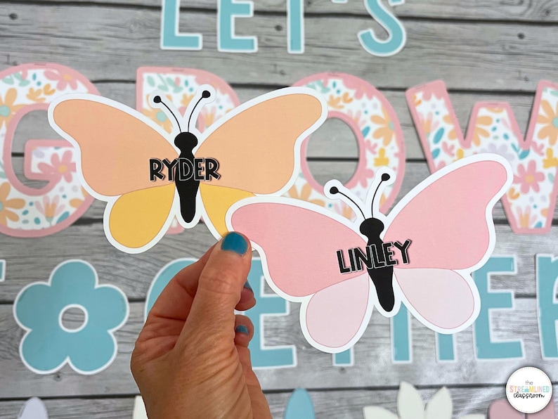 May include: Two pink and yellow butterfly-shaped paper cutouts with the names "Ryder" and "Linley" written on them. The butterflies are on a wooden background with a floral pattern.