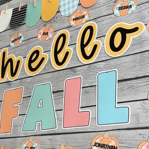 May include: A classroom bulletin board decorated with a fall theme. The board features the words "hello fall" in yellow and black lettering. There are also several pumpkins with names written on them, such as "Hunter", "Maggie", "Ava", and "Sierra".