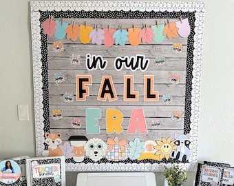 May include: A bulletin board decorated with a fall theme. The board has a wooden background with a white border and black polka dots. The words "in our fall era" are displayed in large, colorful letters. There are also various fall-themed decorations, such as leaves, pumpkins, and animals.
