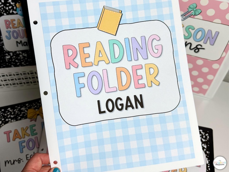 May include: A light blue and white gingham patterned reading folder with the words "READING FOLDER LOGAN" in colorful letters. A small yellow book illustration is above the words. Other folders are visible in the background.