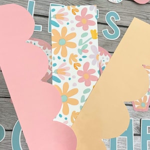 May include: Two scalloped paper borders in pink and peach with a floral pattern in the background. The floral pattern is white with pink, yellow, and blue flowers.