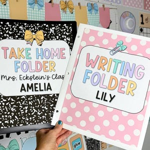 May include: Two school folders. One is black with a white speckled design, the other is pink with white polka dots. The black folder reads "TAKE HOME FOLDER" and the pink folder reads "WRITING FOLDER". Both have the student's name.