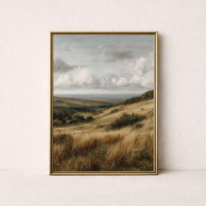 Puede incluir: Pintura de paisaje enmarcada que representa una colina ondulada con hierbas altas y doradas en primer plano. El cielo está lleno de nubes blancas y se ve una masa de agua en la distancia. La obra de arte está en un marco dorado.