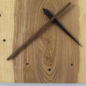 Pu&ograve; includere: Un orologio da parete in legno con finitura a venatura naturale. L'orologio presenta una lancetta delle ore marrone scuro e una lancetta dei minuti nera. Il quadrante dell'orologio ha piccoli indicatori circolari neri.