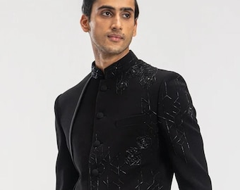Puede incluir: Una chaqueta negra de manga larga con cuello mandarín y un patrón geométrico. La chaqueta tiene un cierre de botón único y se lleva sobre pantalones negros.