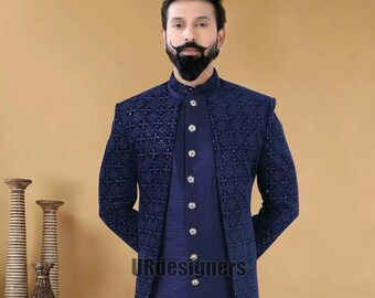 Puede incluir: Una kurta azul marino de manga larga con una chaqueta a juego. La chaqueta tiene un patrón geométrico y está adornada con lentejuelas. La kurta tiene un cuello mandarín y cierre de botones. El modelo lleva pantalones blancos y zapatos blancos.